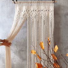 a woman is holding up a white macrame hanging from a wall with orange flowers in front of it