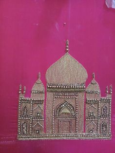 an intricately designed wall hanging on the side of a pink building with gold trim