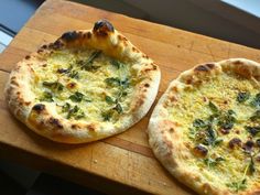 two small pizzas sitting on top of a wooden cutting board next to each other