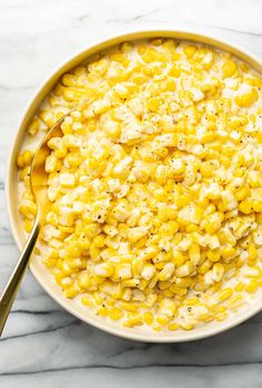 a bowl filled with corn sitting on top of a marble counter next to a spoon