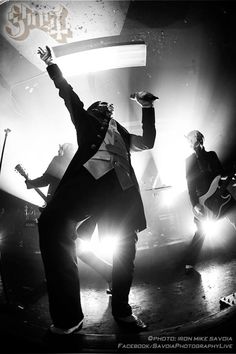 two men on stage with their arms in the air and one man holding his hand up