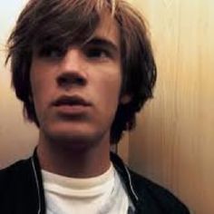 a young man standing in front of a wall with his head turned to the side