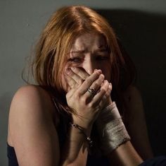 a woman with bandages covering her face and hand in front of her face, sitting on a bed