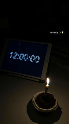 a lit candle sitting in front of a tablet with the date 12 00 on it