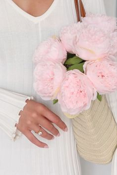 a woman holding a bouquet of pink flowers in her hand and wearing a white sweater