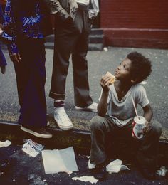 a young boy sitting on the ground eating food next to two women and one man