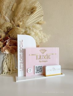 a white table topped with a pink and gold box next to a vase filled with dried flowers