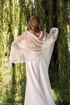 a woman standing in front of a tree wearing a white dress and shawl over her shoulders