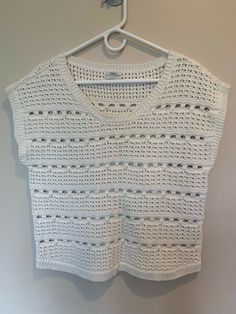 a white crocheted top hanging on a hanger in front of a wall