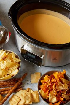 a crock pot filled with soup next to bowls of chips and crackers