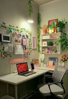 a desk with a laptop computer on top of it next to a plant filled wall