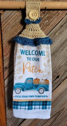 a welcome to our patch kitchen towel hanging on a wooden door hanger with a blue truck and pumpkins