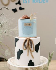 a three tiered cake decorated with black and white cow print, blue ribbon, and brown booties