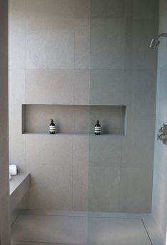 a white tiled bathroom with shelves on the wall and two vases in the shower