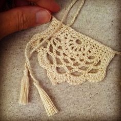 a hand holding a piece of crochet with two tassels on it