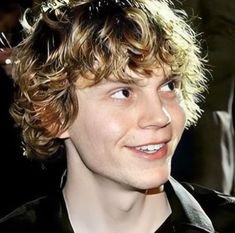 a close up of a person with curly hair and wearing a black shirt smiling at the camera