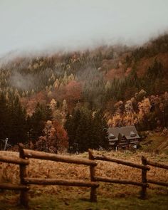 a wooden fence in front of a mountain covered in fog and trees with autumn foliage