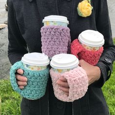 a person holding three coffee cups with crocheted sleeves on their arms and one cup in the other hand