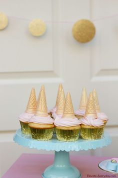 cupcakes with pink frosting and gold cone tops on a blue cake stand