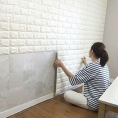 a woman is sitting on the floor and painting a brick wall