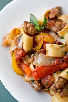 a white plate topped with pasta covered in meat and vegtables on top of it