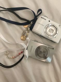 a camera and necklace laying on top of a white bed next to it's strap