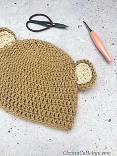 a crocheted bear hat sitting on top of a table next to a pair of scissors