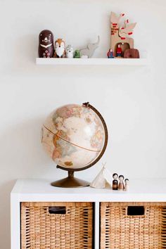 a small globe on top of a white shelf next to wicker baskets and toys