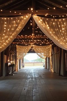 the inside of a barn with lights strung from it's ceiling and sheer curtains