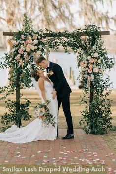 a bride and groom kissing under an arch decorated with flowers