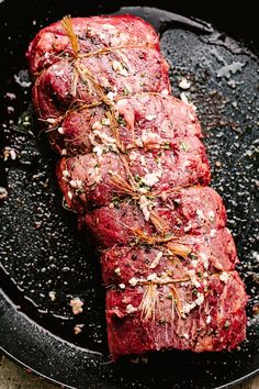 raw meat in a skillet with herbs and seasoning on top, ready to be cooked