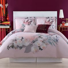 a bed with pink and white flowers on it in front of a purple painted wall