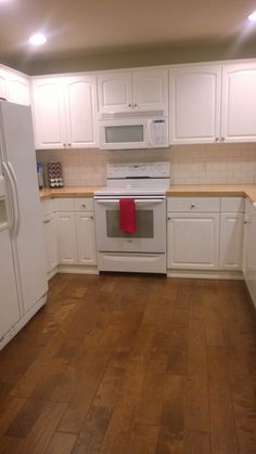 an empty kitchen with white cabinets and wood flooring is seen in this image from the front view