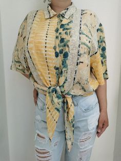 Vintage tie waist button up shirt from the 1990's. Women's short sleeve button up blouse with a tie waist. Beautiful 90's print in tones of yellow, beige, black and green. Oversized fit. Material: Tag has faded. Feels like viscose. Size: Marked 48 DE, which is 18 US or XL. Model on the second photo is 40 DE or L. To be sure this item would fit you, please look at the measurements below. Approximate measurements (taken when shirt is lying flat, double armpit to armpit and waist): Shoulder to shou Casual Short Sleeve Blouse With Tie Sleeves, Casual Blouse With Tie Sleeves, Casual Summer Shirt With Tie Sleeves, Casual Short Sleeve Blouse With Tie Waist, Casual Tops With Tie Sleeves And Short Sleeve, Spring Button-up Tops With Tie Waist, Summer Short Sleeve Blouse With Tie Sleeves, Casual Tops With Tie Sleeves, Summer Blouse With Tie Sleeves And Short Sleeve