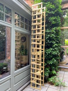 a tall wooden trellis sitting next to a green planter in front of a window