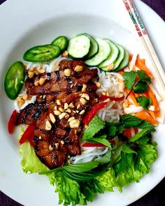 a white plate topped with meat, veggies and noodles next to chopsticks