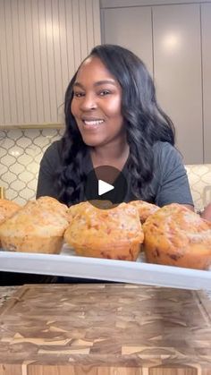 a woman sitting in front of a tray filled with muffins on top of a counter