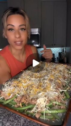 a woman holding a tray with food on it and pointing to the camera while smiling