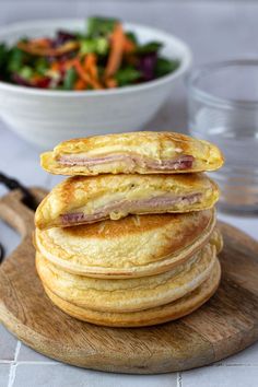 a stack of pancakes sitting on top of a wooden cutting board next to a bowl of salad