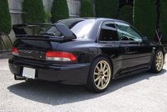 a black car with gold rims parked in a parking lot next to some bushes