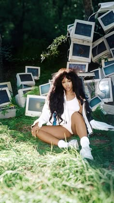 a woman sitting on the ground surrounded by computer monitors and televisions in an open field