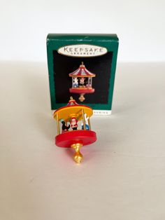 a small toy carousel with people on it in front of a green box and white background