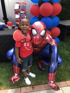 a young boy standing next to a spider man balloon sculpture in front of a party table