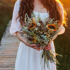 a woman holding a bouquet of flowers in her hands while standing on a wooden walkway