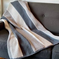 a gray and white blanket sitting on top of a black couch next to a window