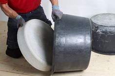 a man in red shirt and gloves holding a large metal object on top of a wooden table