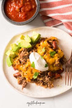 an enchilada on a plate next to a fork and bowl of salsa