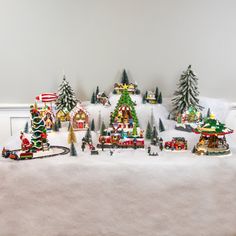 a christmas village is shown in the middle of a snow - covered area with trees and train tracks