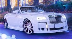 a white rolls royce parked in front of some trees