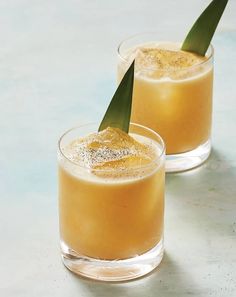 two glasses filled with orange juice and garnished with a green leaf on top